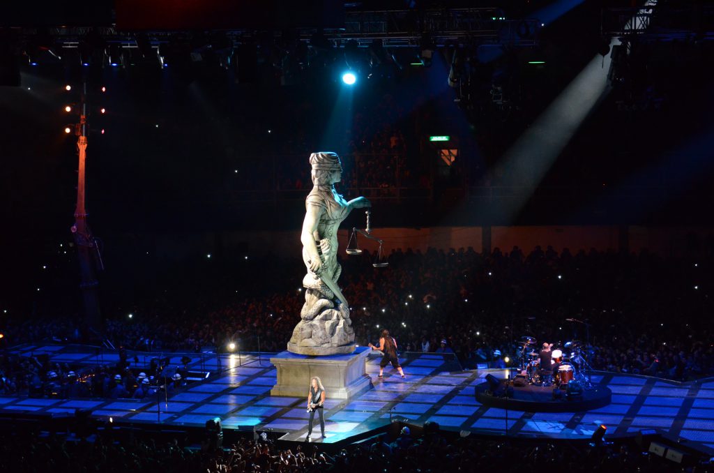 A photo of Metallica performing underneath the statue of justice on the Through the Never tour stage